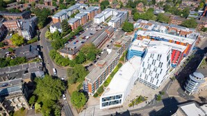Vue aérienne d’une zone commerciale avec des bâtiments modernes, des parkings et des espaces verts.