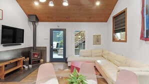 Ein modernes Wohnzimmer mit Holzboden, einem an der Wand befestigten Fernseher, einer Couch, einem Glastisch mit Pflanze und einem Kamin.