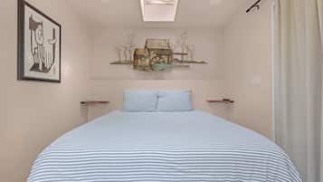 Een slaapkamer met een bed, een lijstwerk kunstwerk, een plafondlamp en een wandplank met een schilderij van een rustieke watermolen.