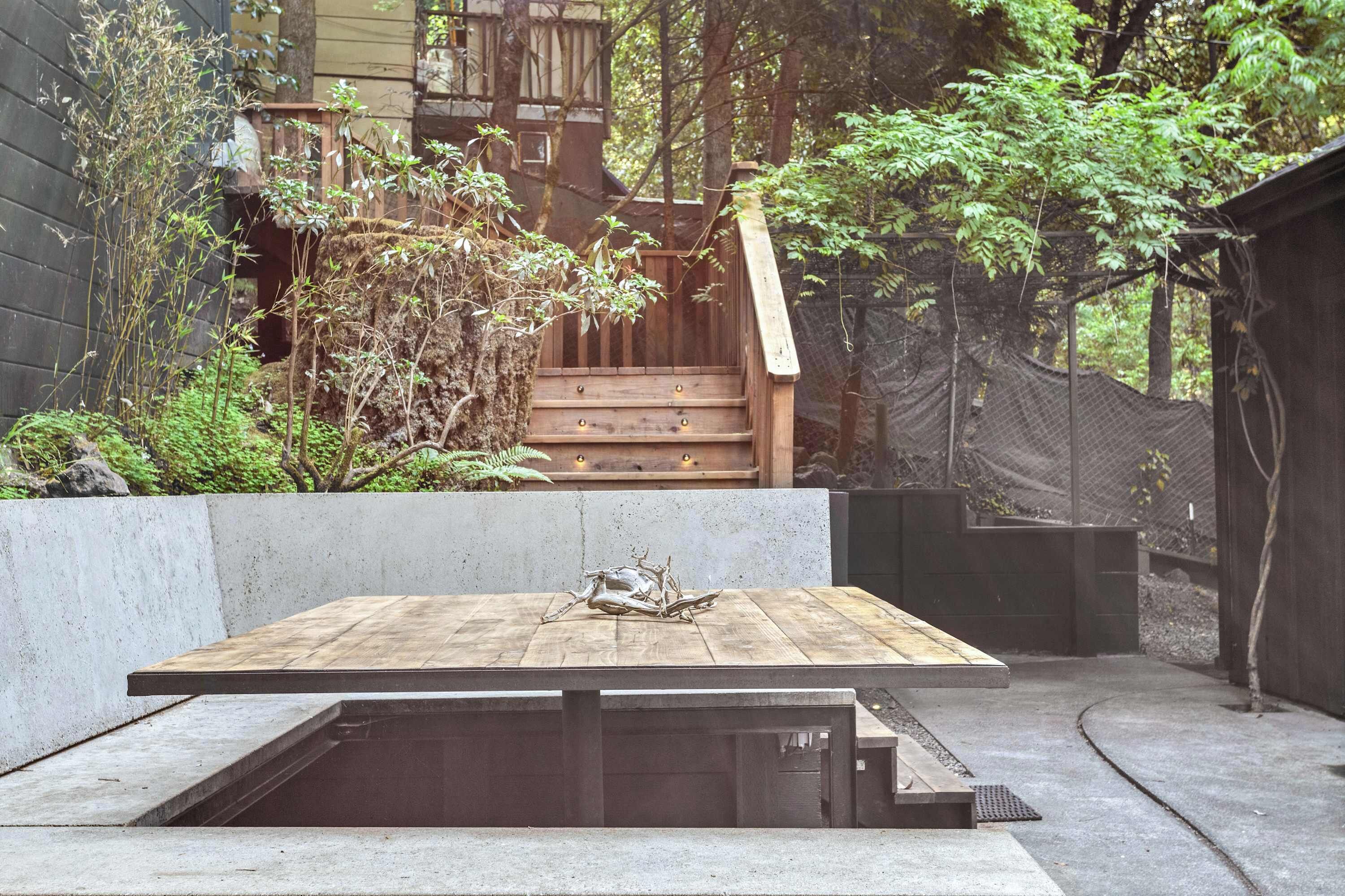 A wooden deck with a bench, surrounded by greenery and a staircase leading to a wooden structure.