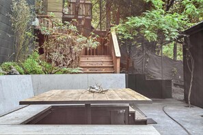 A wooden deck with a bench, surrounded by greenery and a staircase leading to a wooden structure.