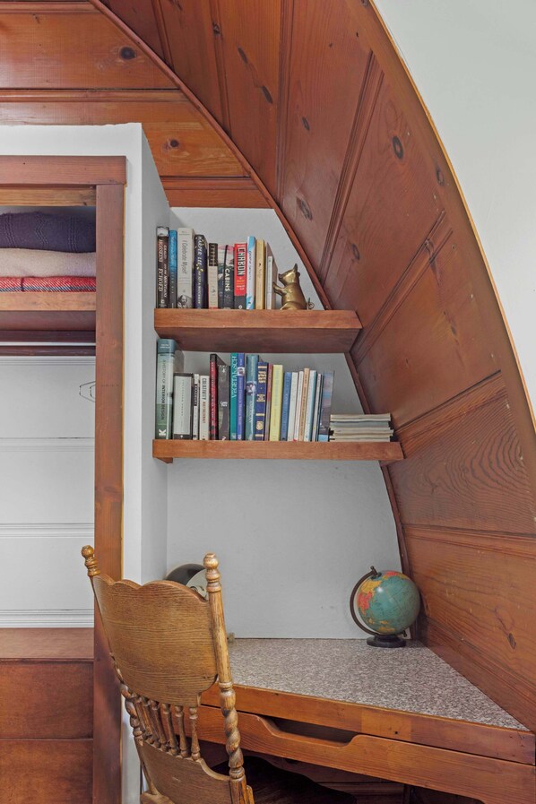 Un escritorio de madera con un globo terráqueo y libros, una silla de madera y una estantería llena de libros.