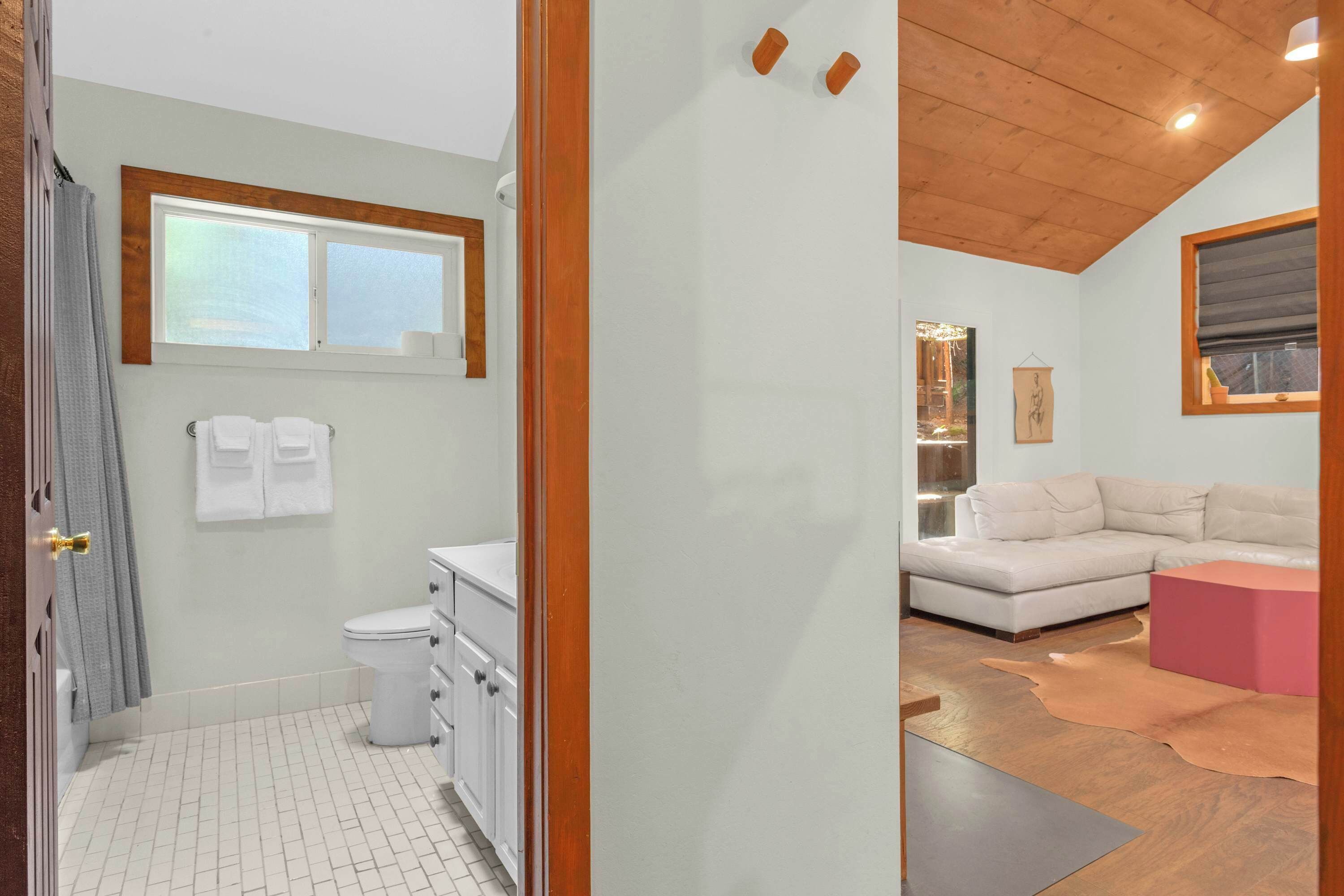 A modern bathroom with a toilet, sink, and towel rack. There is a wooden ceiling and a window above the sink.