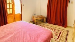 A bedroom with a bed, a ceiling fan, a small table, a red curtain, and a window with curtains.