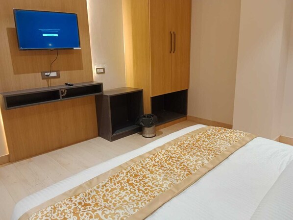 A hotel room with a bed, a television mounted on the wall, a desk, and a wardrobe.