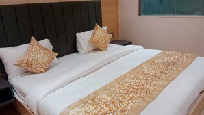 A neatly made bed with a patterned bedspread and pillows, a wooden headboard, and a nightstand with a lamp. - Sampanna Inn (Varanasi)