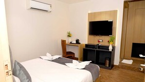 A hotel room with a bed, a desk, a chair, a TV, and a fireplace. - Sampanna Inn (Varanasi)