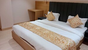 A neatly made bed with a patterned bedspread, two pillows, and a bedside table with a lamp. - Sampanna Inn (Varanasi)