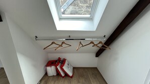 Una habitación pequeña con techo inclinado, tragaluz, piso de madera y un perchero con ganchos.