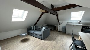 Un apartamento estilo loft con cama en altillo, un sofá gris, una mesa de comedor con sillas, una mesita redonda y una zona de cocina.
