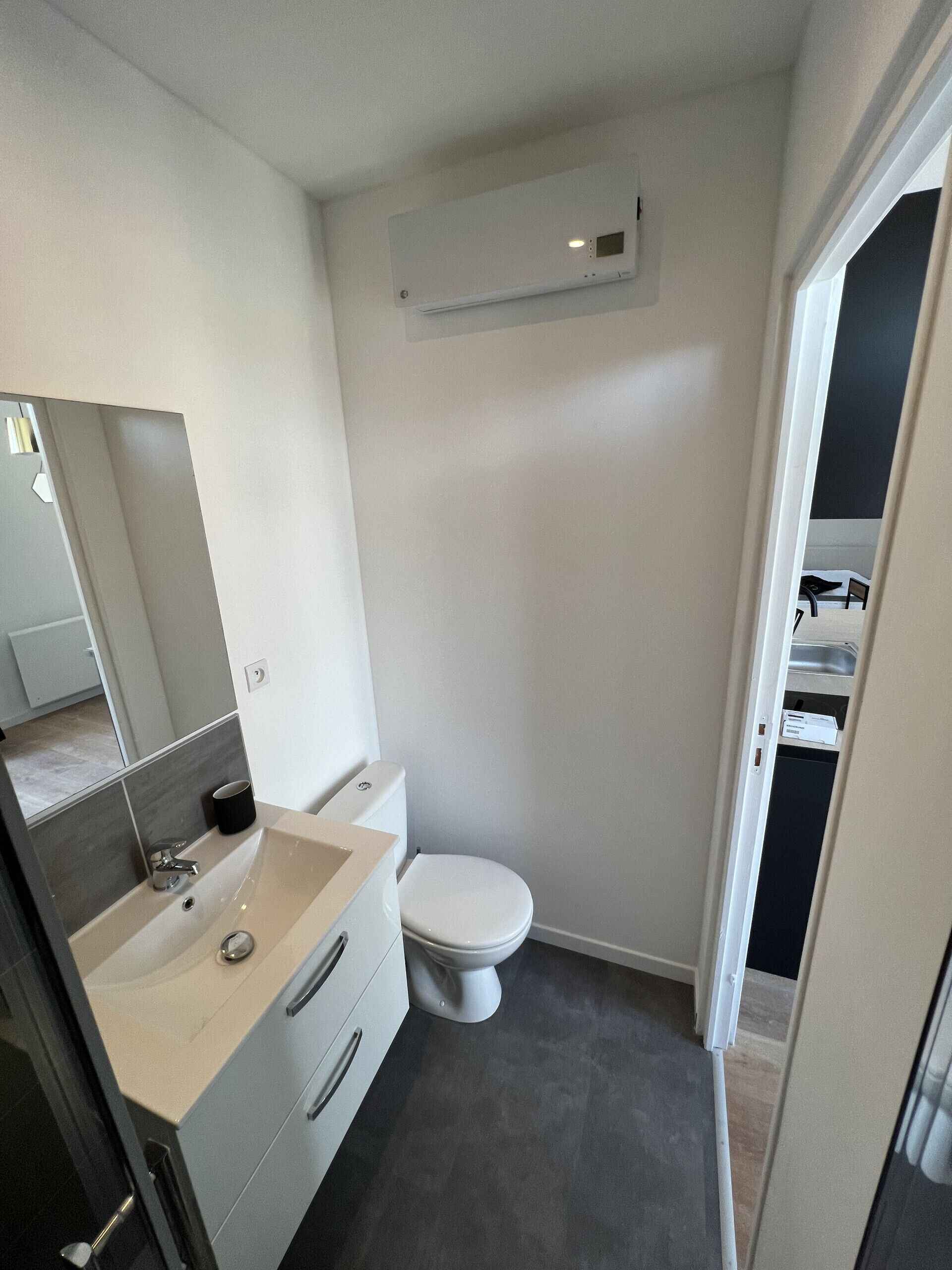 Un baño pequeño con inodoro blanco, lavamanos con espejo y una ventana.