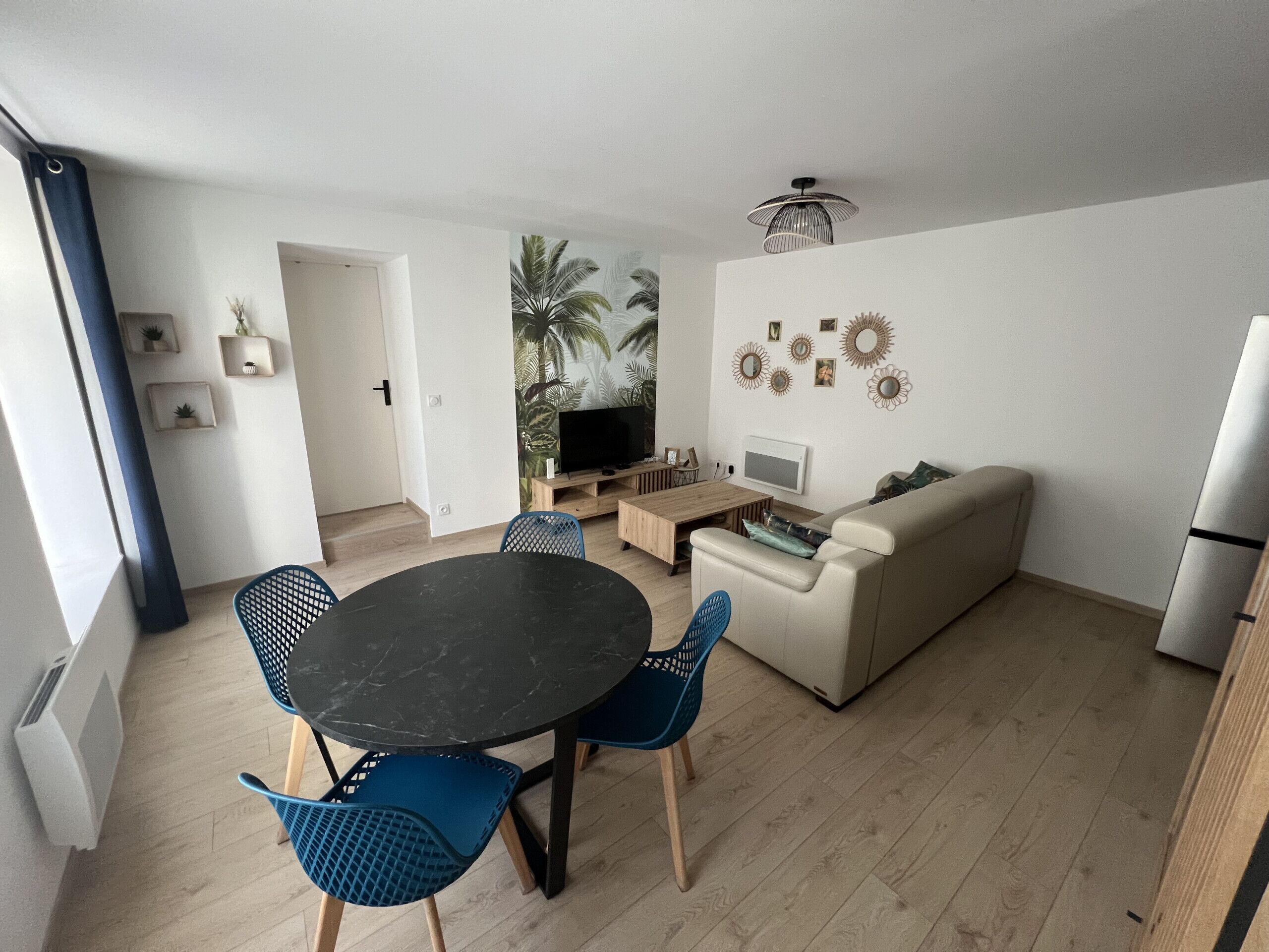 A modern living room with a black dining table, blue chairs, a beige sofa, and a TV.