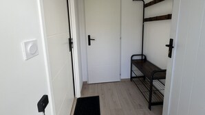 Un corridoio stretto con una porta bianca, una panca nera e un mobiletto a scaffali in metallo addossato alla parete.