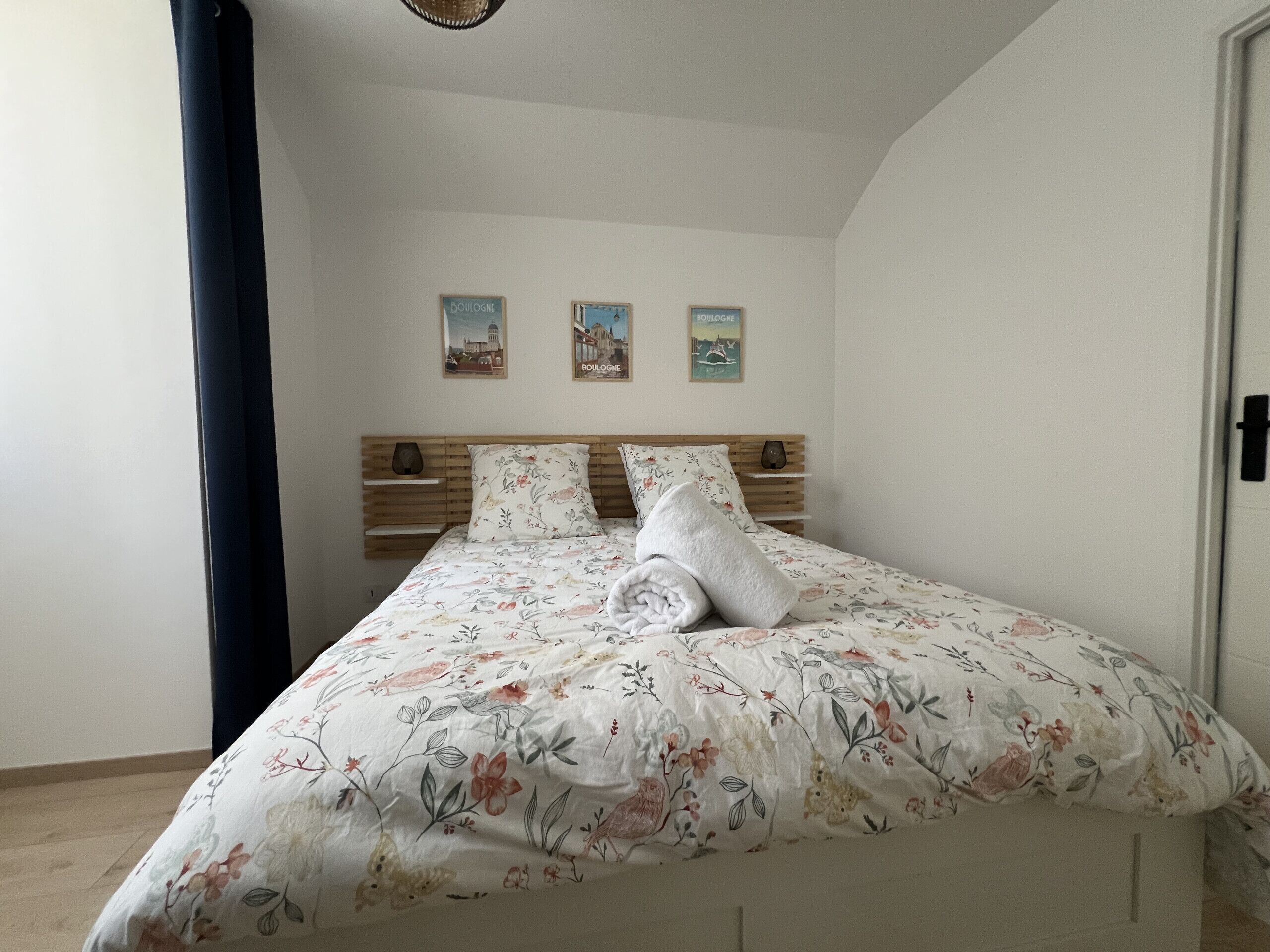 A neatly made bed with floral bedding, a wooden headboard, and two wall-mounted pictures.