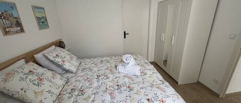 A bedroom with a floral bedspread, a neatly made bed, a wardrobe, and two wall posters.