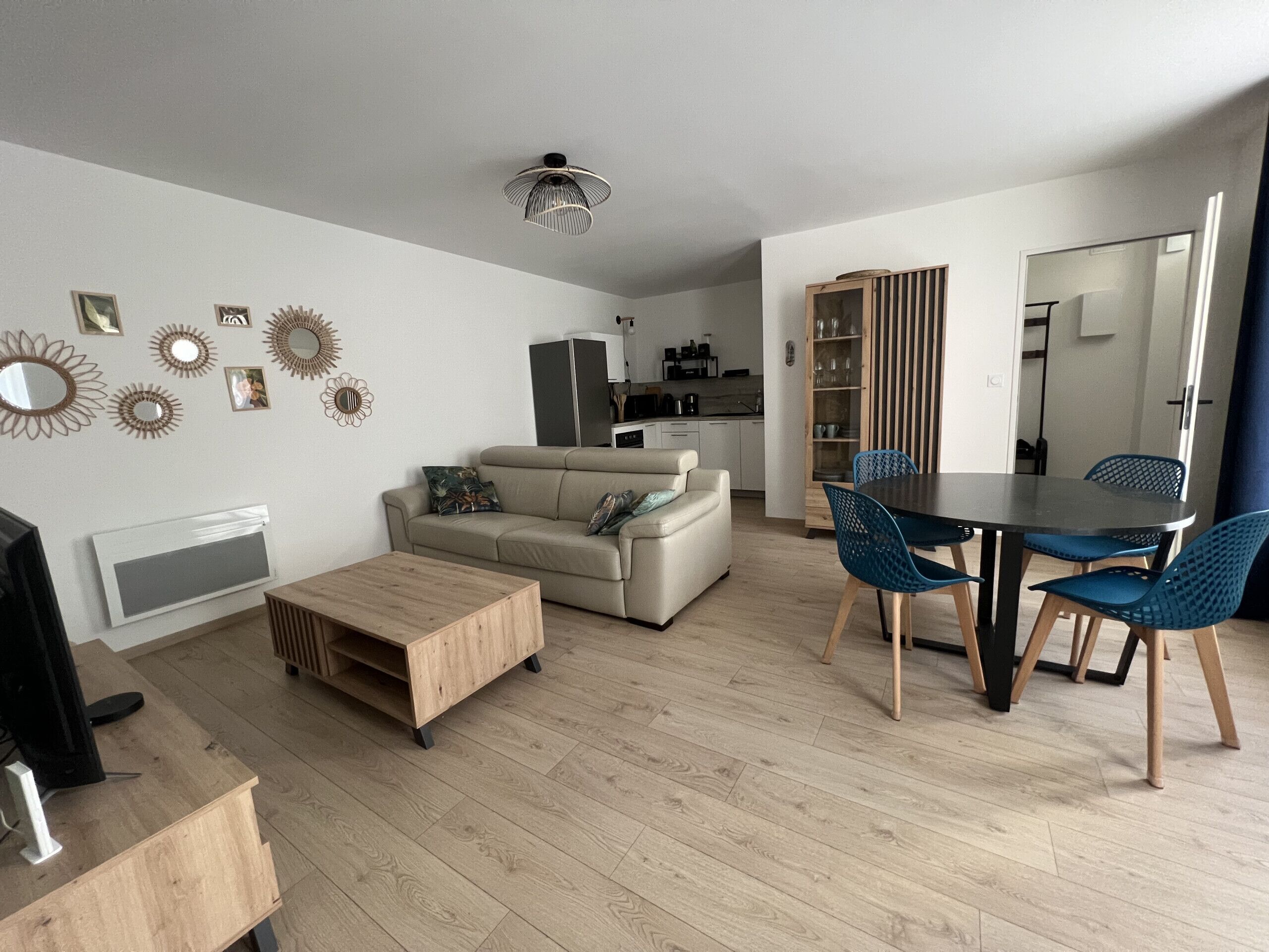 Un salon moderne avec un canapé, une table basse et un coin repas avec des chaises. On aperçoit une cuisine au fond.