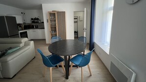 Un soggiorno moderno con un tavolo rotondo, due poltrone blu, un divano e una cucina sullo sfondo.