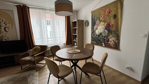 Ein Essbereich mit einem runden Tisch, sechs Stühlen, einer Pendelleuchte, einem Fernseher und einem großen Blumenbild an der Wand.