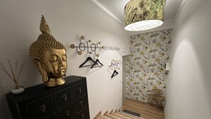 Eine Treppe mit Holzvertäfelung, eine schwarze Aufbewahrungseinheit mit mehreren Schubladen, ein dekorativer Buddha-Kopf, Wandbilder und eine Wandtapete mit Muster.