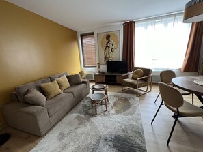Olohuoneessa on sohva, sohvapöytä, televisio sekä ruokailutila, jossa on tuoleja ja pöytä.