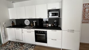 Eine moderne Küche mit weißen Schränken, einer schwarzen Arbeitsplatte, einer Mikrowelle, einer Kaffeemaschine und einem Backofen.