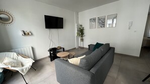 A modern living room with a grey sofa, a small round table, a flat-screen TV mounted on the wall, and a potted plant. - A 2 pas du Beffroi, 2-4p Wifi, Parking (Boulogne-sur-Mer)