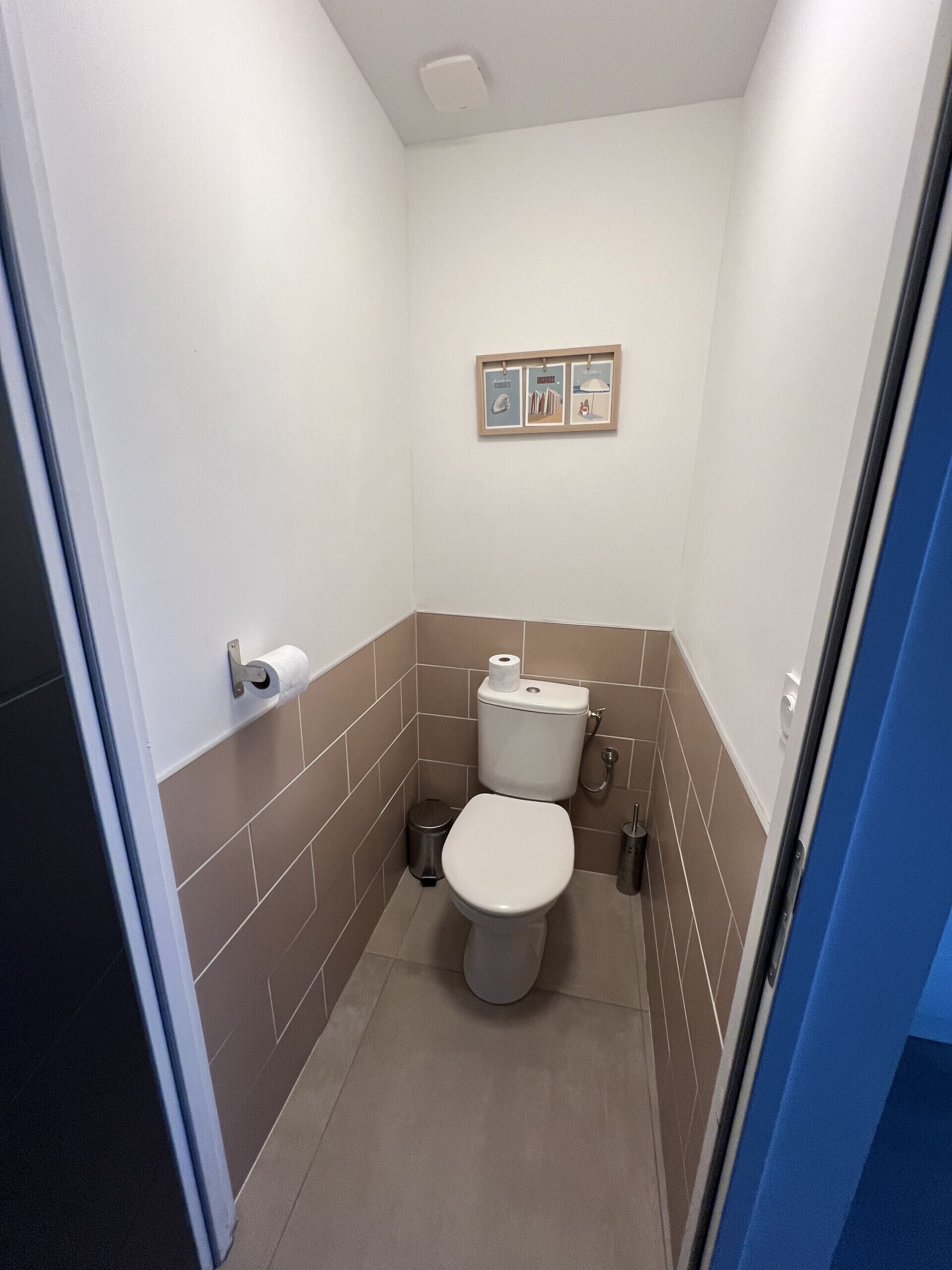 A small, compact bathroom with a toilet, a trash bin, and a wall-mounted toilet paper holder.