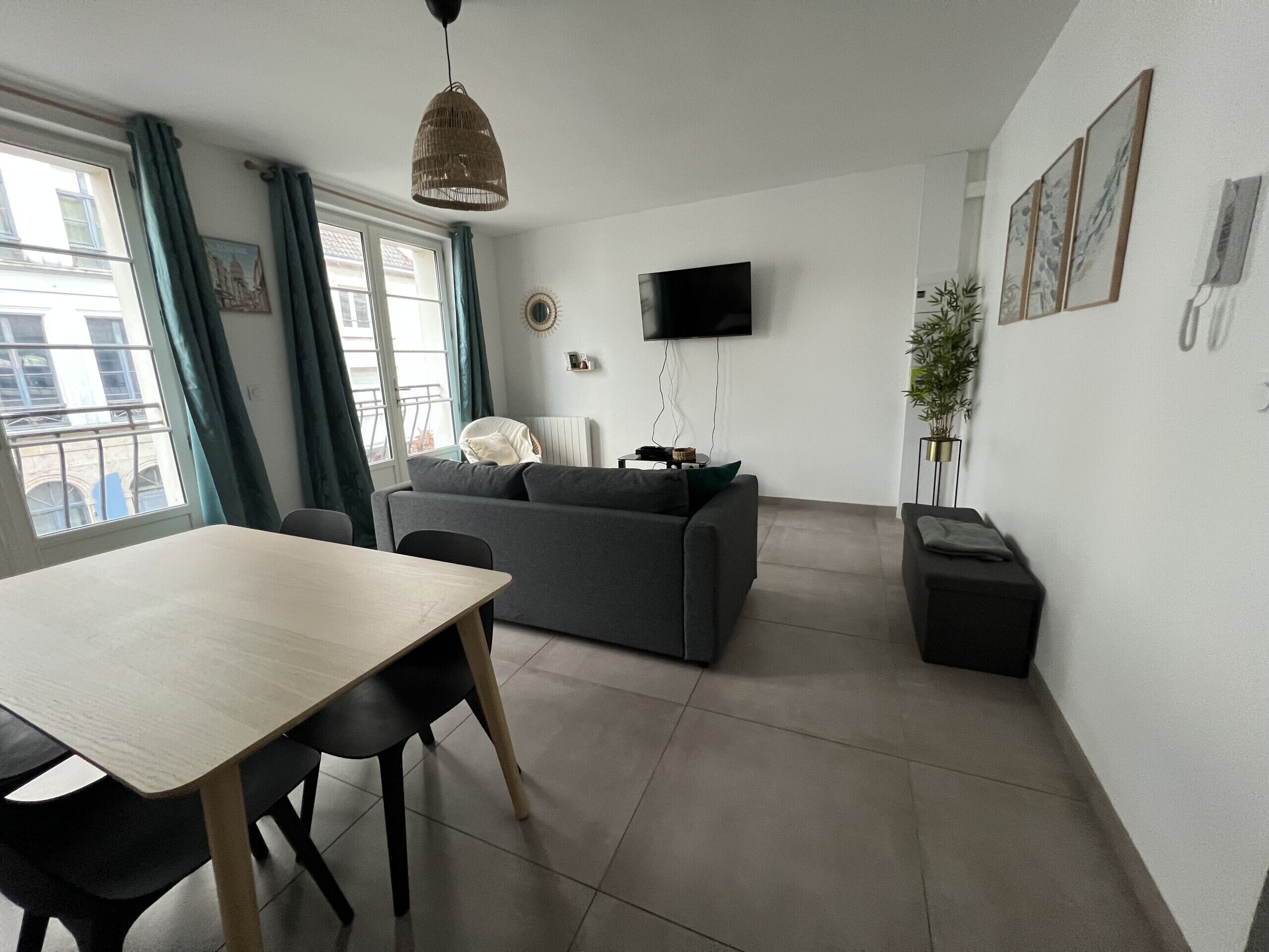 A modern living room with a sofa, a dining table, chairs, a TV, and a plant.