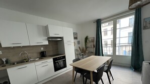 A modern kitchen with white cabinets, a black stove, and a dining area with a wooden table and chairs. - A 2 pas du Beffroi, 2-4p Wifi, Parking (Boulogne-sur-Mer)