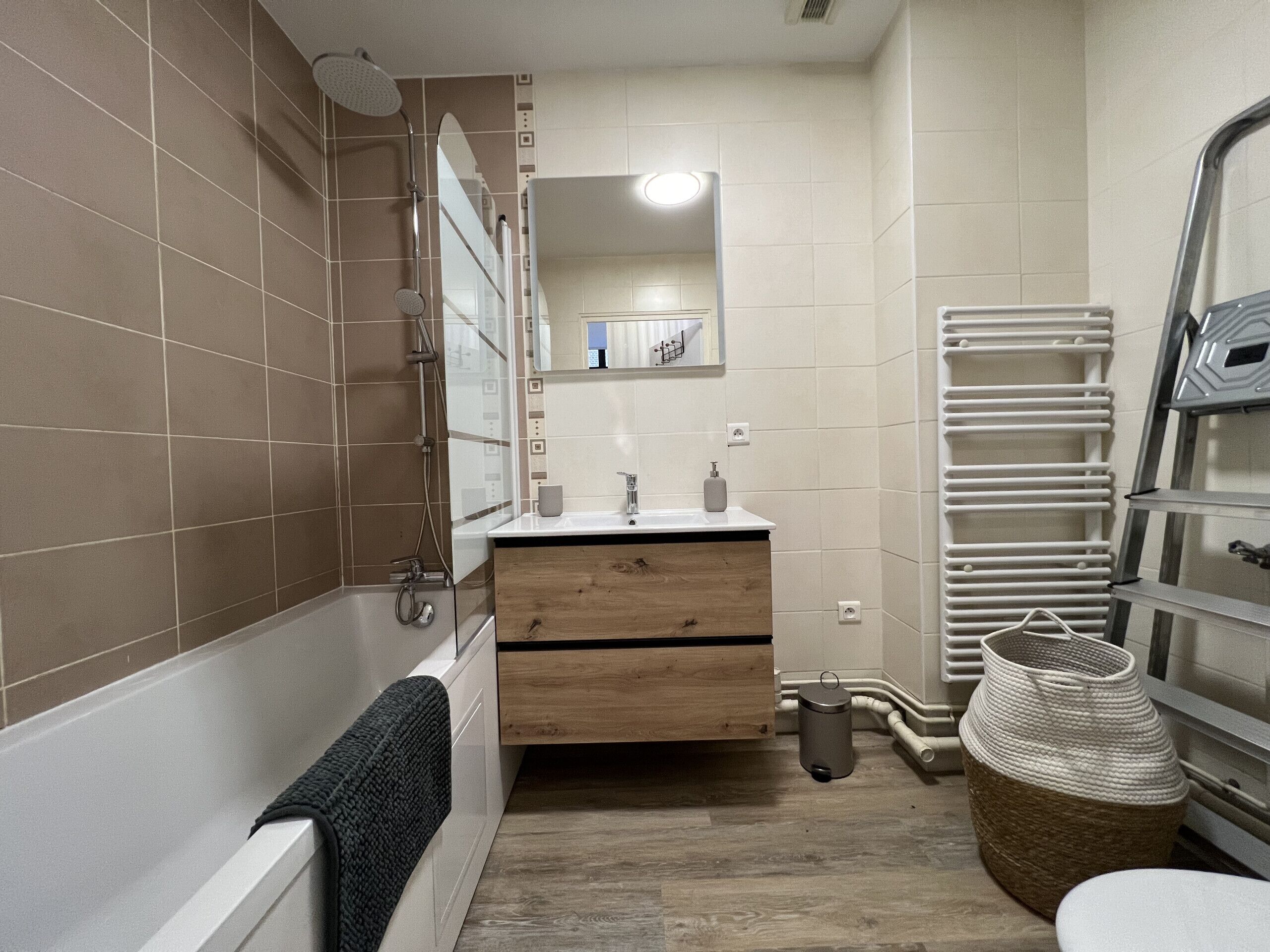 Un bagno con una vasca, un lavandino con uno specchio sopra, un portascopevoli e un cestino.