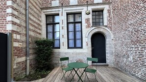 A courtyard with a wooden deck, two green folding chairs, and a black door.