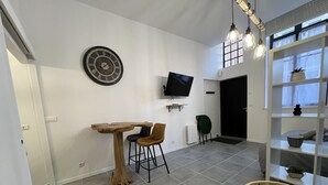A modern living room with a wooden table, two chairs, a television, a decorative clock, and a wicker basket.