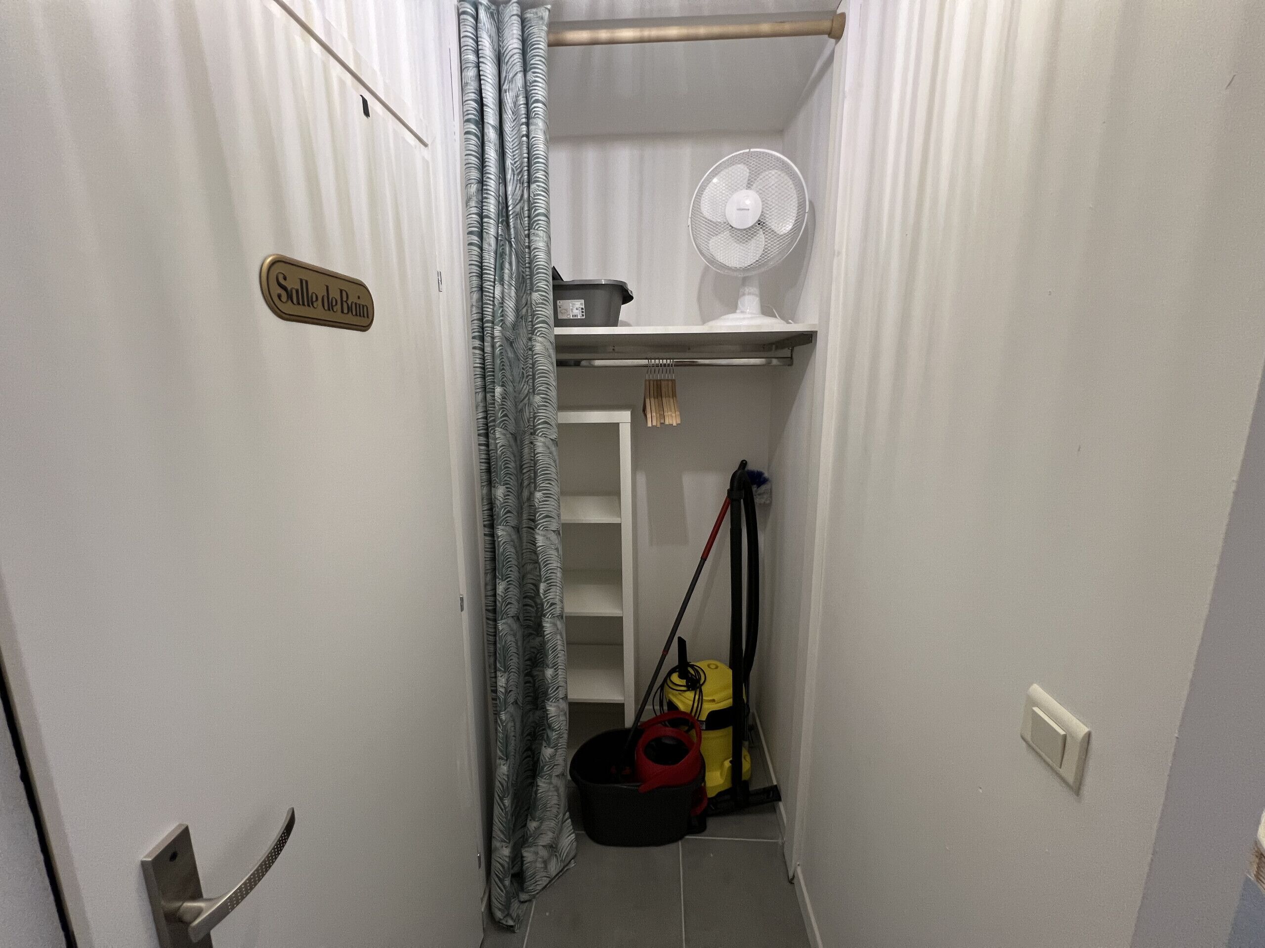 A narrow hallway with a shower curtain, a fan, and cleaning equipment.
