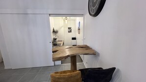 A modern kitchen with a wooden table and two chairs, a clock on the wall, and a view into the dining area.