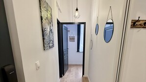 A hallway with a wooden floor, white walls, and a door at the end. There are wall-mounted lights and a ceiling light. - Le Calais Wilson 1 : 4 pers (Calais)