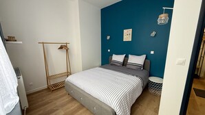 A bedroom with a bed, a wooden wardrobe, a radiator, and a blue accent wall. - Le Calais Wilson 1 : 4 pers (Calais)