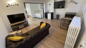 A modern living room with a black sofa, a flat-screen TV, and a dining area with a small table and chairs.