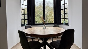 Ein runder Holztisch mit vier Stühlen vor einem Erkerfenster mit schwarzen Rahmen.