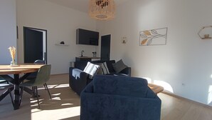 Ein modernes Wohnzimmer mit Essbereich, einer Couch, einem Couchtisch und einer Küchenzeile im Hintergrund.