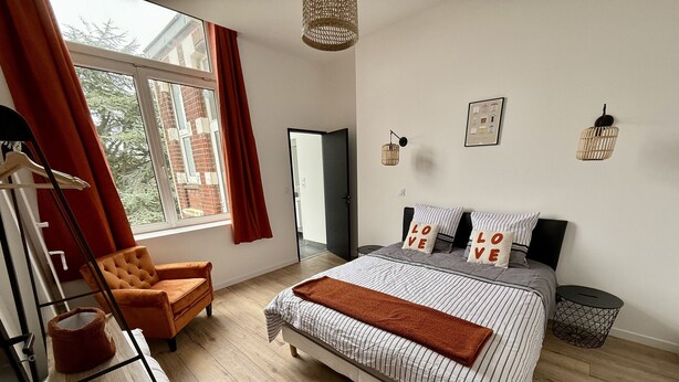 A bedroom with a bed, a chair, a wardrobe, and a window with curtains. - Le Calais Wilson 6 : Appt 4p (Calais)