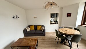 A modern living room with a dark grey sofa, yellow cushions, a wooden coffee table, and a round dining table with chairs. - Le Calais Wilson 6 : Appt 4p (Calais)