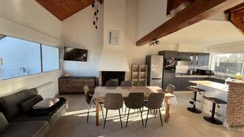 A spacious living area with a dining table, chairs, a sofa, a fireplace, and a kitchen in the background.