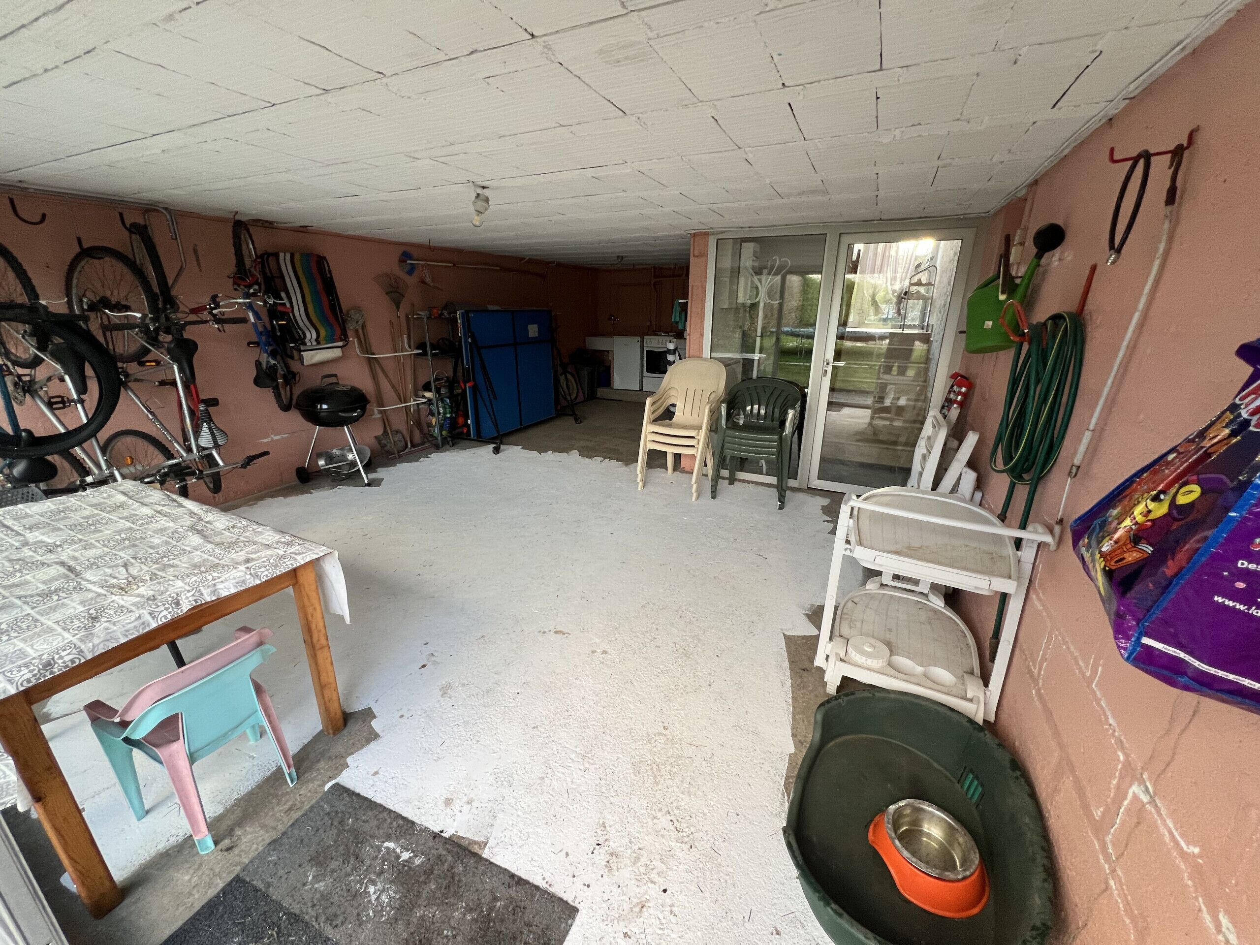 Eine Garage mit Tisch, Stühlen, einem Fahrrad und einer Hundeschüssel.