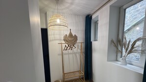 Ein Flur mit Holzboden, einer Pendelleuchte, einem Wandregal und einem Fenster mit Blick auf Bäume.