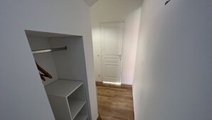 Un couloir étroit doté d’un plancher en bois, une porte blanche au fond et un placard avec des étagères et une tringle pour suspendre les vêtements.