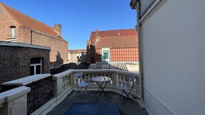 Une ruelle étroite avec un petit balcon agrémenté d’une table et de chaises.