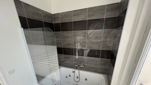 Une salle de bain moderne avec une baignoire sur pieds, des murs recouverts de carreaux foncés et une fenêtre.