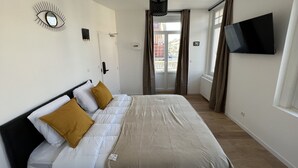 A hotel room with a bed, a TV mounted on the wall, and a view of the outside through the window. - La Suite Balnéo - 2p downtown Liévin (Liévin)