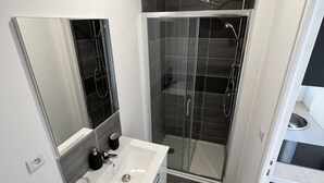 A modern bathroom with a white vanity, a glass shower enclosure, and a mirror above the sink. - Vue sur les Toits - 2p downtown Liévin (Liévin)