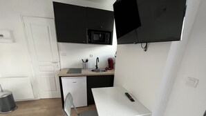 A compact kitchen with a microwave, sink, and a small refrigerator. There is a foldable chair and a white table with a remote control on it. - Vue sur les Toits - 2p downtown Liévin (Liévin)